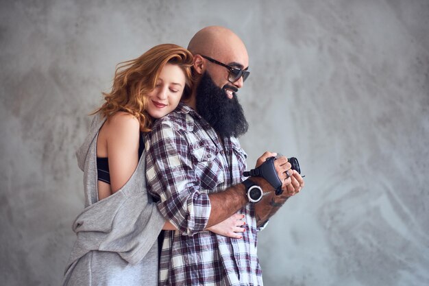 Amateur bearded photographer and a redhead female posing over light grey background.