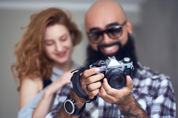 Amateur bearded photographer and a redhead female posing over light grey background.