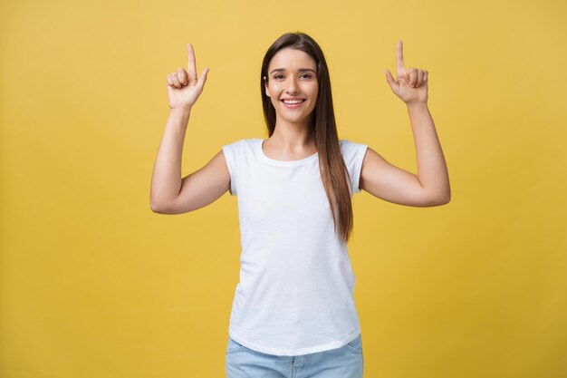 Amaze young woman pointing to one side with her finger while opening her mouth against a yellow background