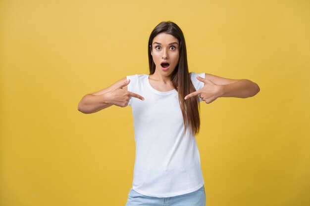 Amaze young woman pointing to one side with her finger while opening her mouth against a yellow background.