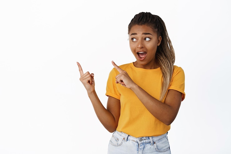Free Photo amazed african american girl pointing and looking at upper left corner with impressed face excitement over advertisement sale white background