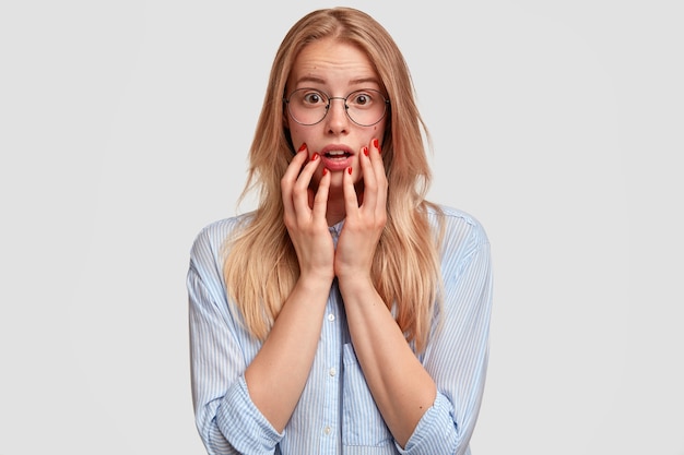 amazed beautiful woman with astonished expression, has worried look, feels horror because of something terrified, keeps hands near mouth