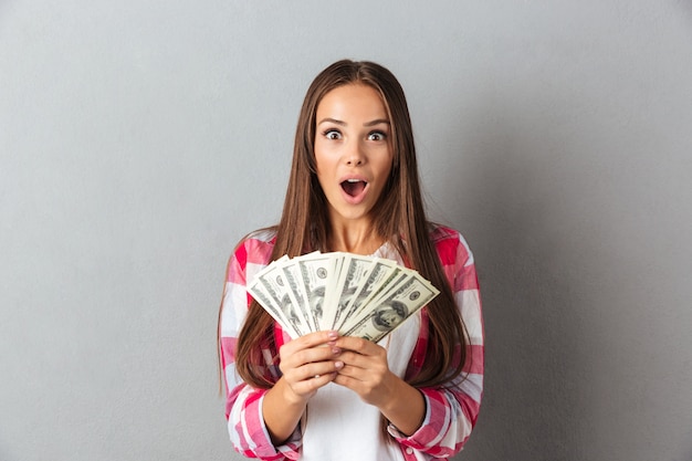 Free photo amazed beautiful young brunette woman in checkered shirt holding money