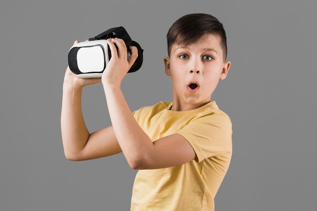Удивленный мальчик держит гарнитуру виртуальной реальности