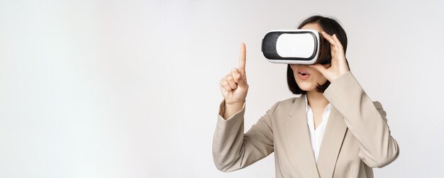 Amazed business woman in suit using virtual reality glasses looking amazed in vr headset standing over white background