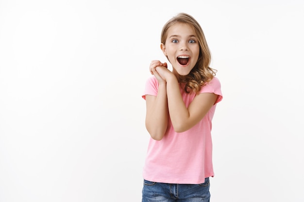 Free photo amazed cute little kid see wonderful thing, clasp hands joyfully excited and admiration look camera, smiling broadly amused, gazing entertained and surprised, receive cool gift, white wall