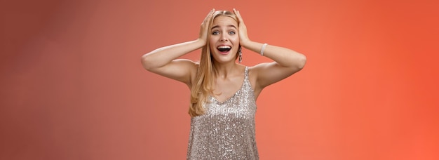 Amazed excited nervous young beautiful blond woman in silver stylish dress cannot believe own luck