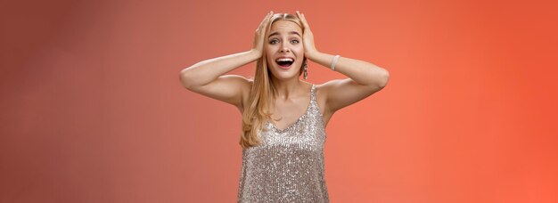 Amazed excited nervous young beautiful blond woman in silver stylish dress cannot believe own luck
