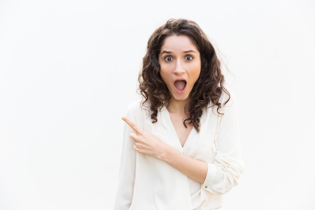 Amazed excited woman with open mouth pointing finger away