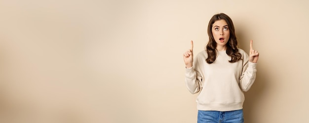 Free photo amazed girl checking out banner announcement reading promo text upwards pointing fingers up standing