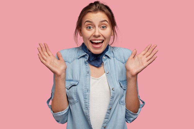 Amazed joyful Caucasian female spreads palms, being excited by good news, has toothy smile