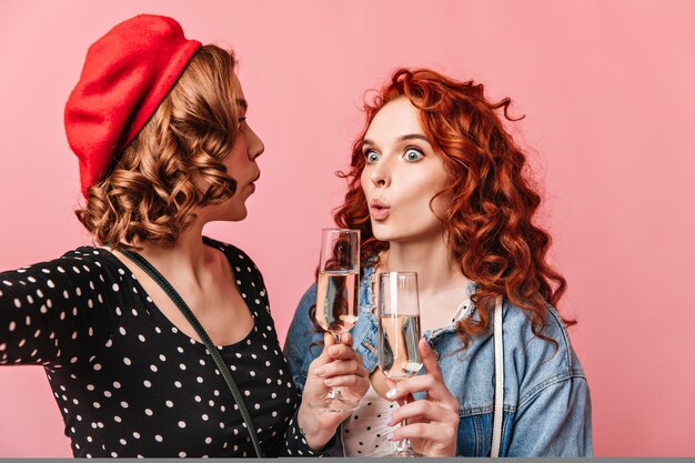 シャンパンを飲んで驚いた女性。ピンクの背景にワイングラスを持って驚いた女の子のスタジオショット。