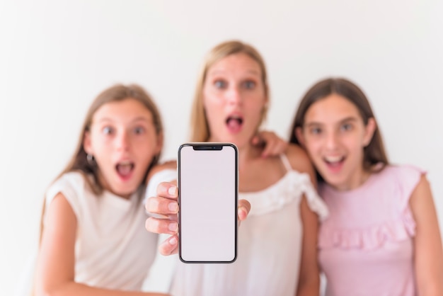 Amazed mother and daughters holding smartphone with blank screen 