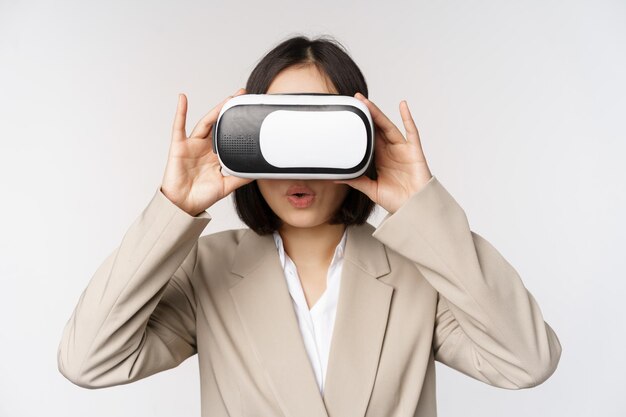 Amazed office woman asian business person in suit wearing vr headset looking at smth in virtual reality glasses with impressed wow face white background