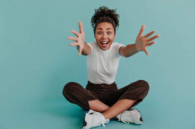 Free photo amazed pretty woman posing with outstretched hands on turquoise wall