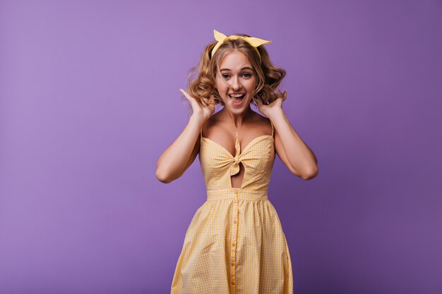 Amazed romantic girl jumping on purple. Portrait of inspired lady in yellow dress fooling around in leisure time.