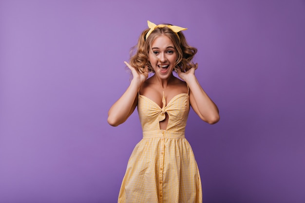 Пораженная романтическая девушка прыгает на фиолетовом. Портрет вдохновленной дамы в желтом платье, дурачящейся в свободное время.
