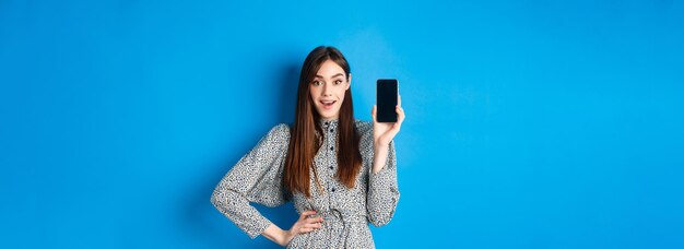 Amazed smiling woman showing empty smartphone screen look impressed recommending online promo blue b