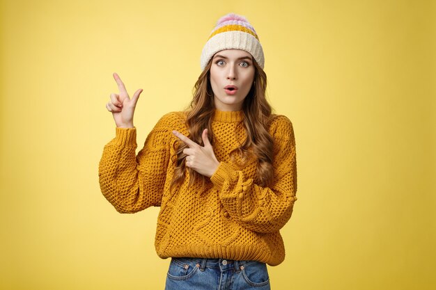 Amazed speechless stunned cute fashionable girl fold lips say wow widen eyes surprised impressed pointing upper left corner curious what promotion shows, look you questioned, yellow background