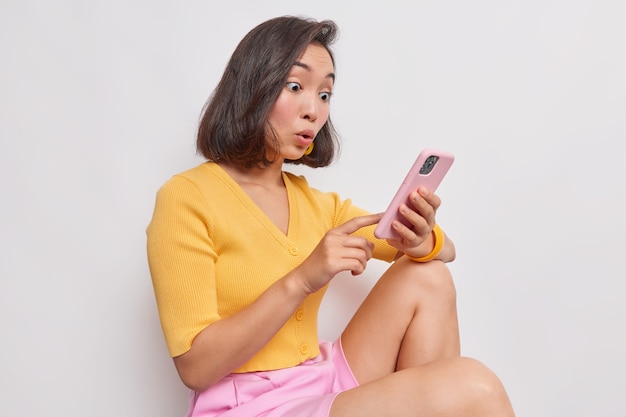 Amazed surprised asian woman stares at smartphone received bank debt notification reads sms with unbelievable news makes big eyes excited by online lottery win job promotion or great shopping offer