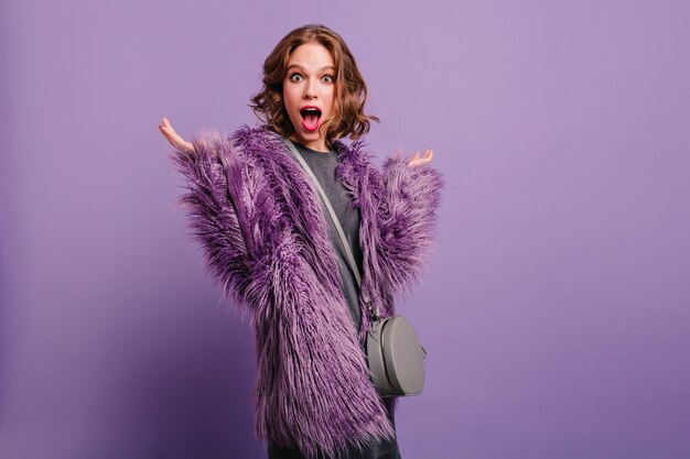 Amazed white lady with beautiful eyes posing with hands up on purple background