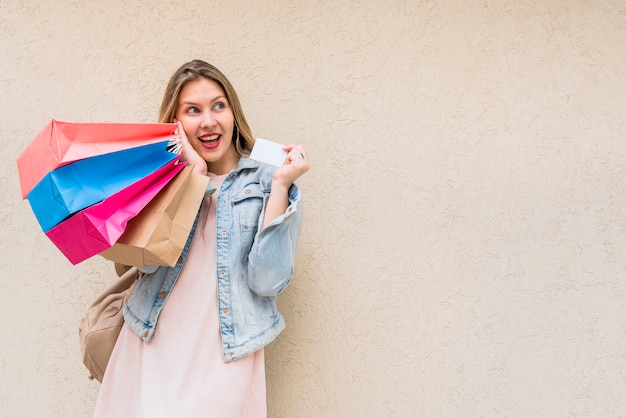 Free photo amazed woman standing with shopping bags and credit card at wall