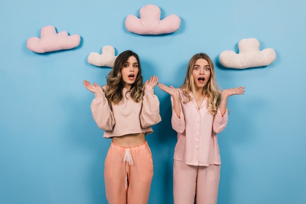 Amazed women in cute pajamas posing with hands up