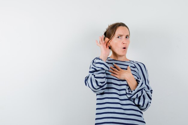 Amazed young girl doing a hard of hearing gesture on white background