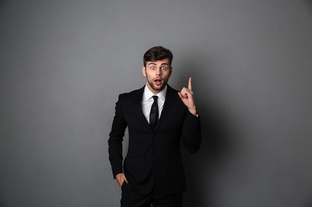 Amazed young man in suit pointing with finger upward, 