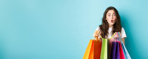 Free photo amazed young woman shopaholic holding colorful shopping bags and look amused at next shop buying thi