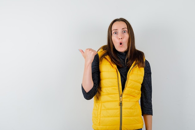 Amazed young woman showing the left back with her thumb on white background