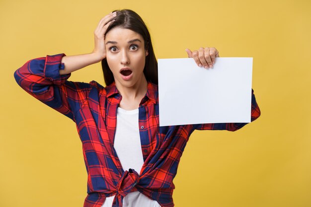 Amazement or surprised female with blank white panel, isolated on yellow background.