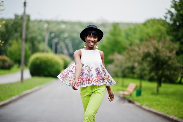 공원에서 다른 감정을 가진 녹색 바지와 검은 모자를 쓴 놀라운 아프리카계 미국인 모델 여성