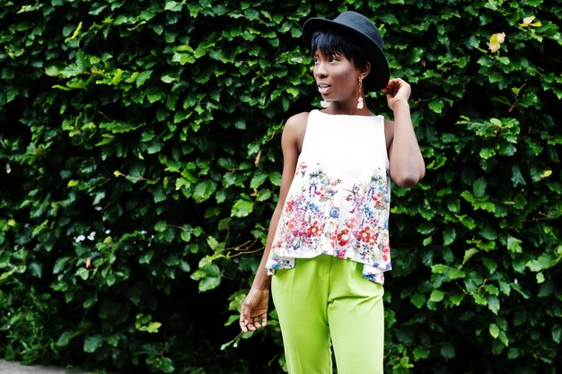 Amazing african american model woman in green pants and black hat posed with different emotions at park