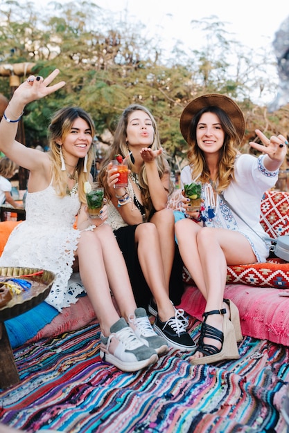 Free photo amazing blonde girl sending air kiss, while her charming friends laughing and showing peace sign