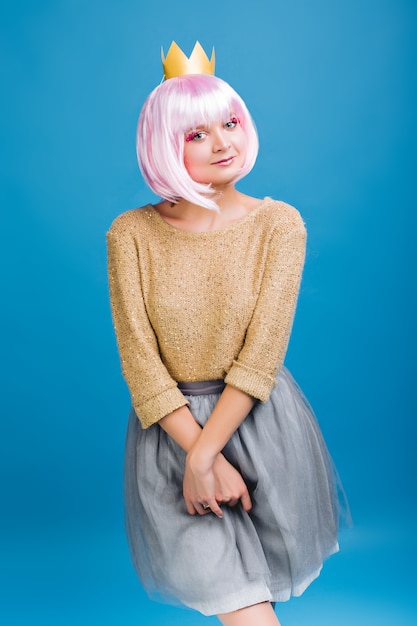 Amazing cheerful young woman in luxury clothes . Cut pink hair, golden sweater, grey tulle skirt, crown on head, positive face emotions, celebrating new year party, birthday.