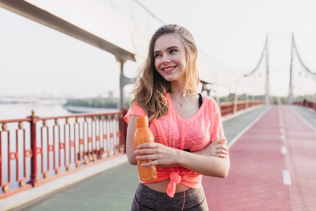 Amazing european girl posing at stadium with cute smile. Outdoor shot of lovely young woman laughing after training.