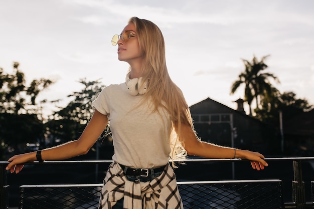 Amazing fair-haired woman in casual attire standing on the street in evening.