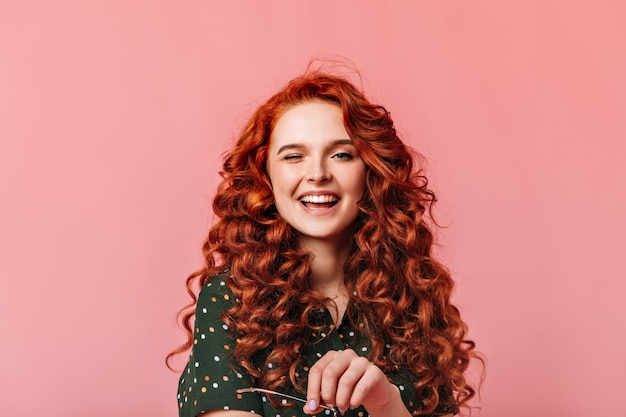 Amazing ginger lady laughing at camera. Front view of attractive curly girl isolated on pink background.