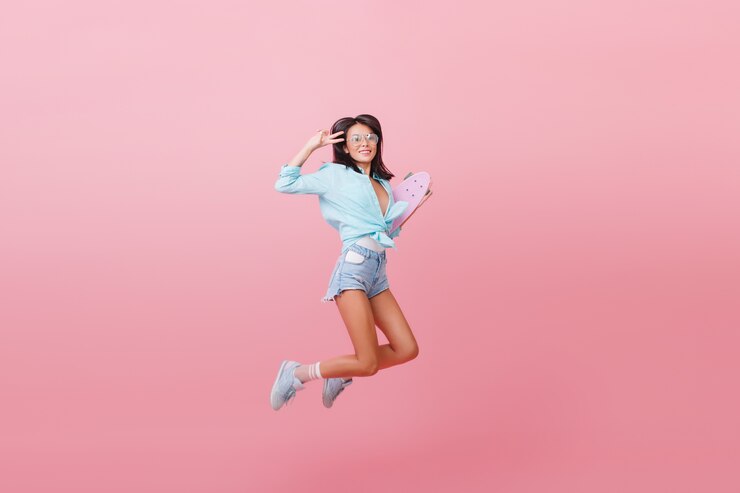 無料Photo スケートボードでジャンプするストリートの衣装で素晴らしいラテンファッショナブルな女の子。ジーンズのショートパンツとストライプの靴下を楽しんでいるトレンディな女性