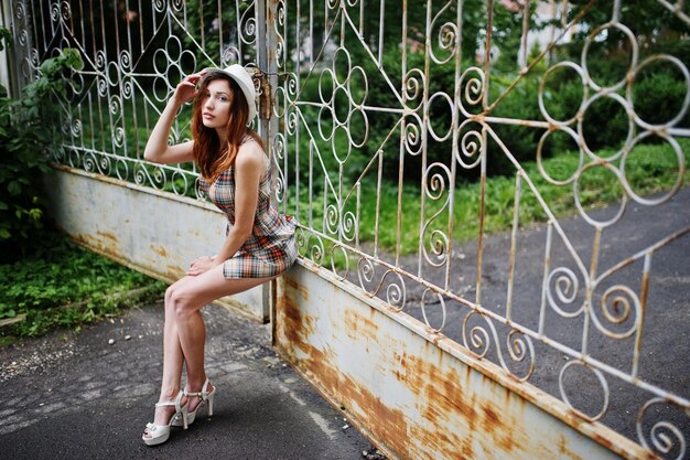 Amazing long legs with hig heels girl wear on hat against iron fence