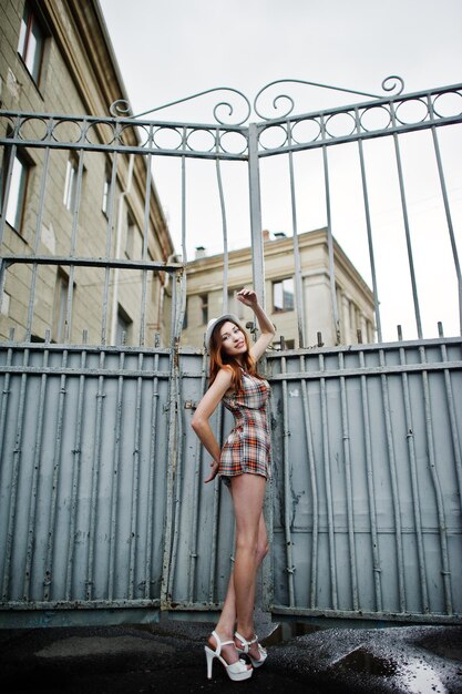 Amazing long legs with hig heels girl wear on hat against iron fence