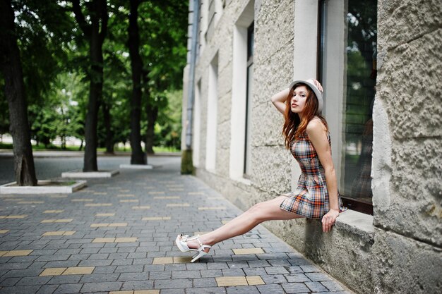 Amazing long legs with hig heels girl wear on hat sitting on the window sill on streets of city