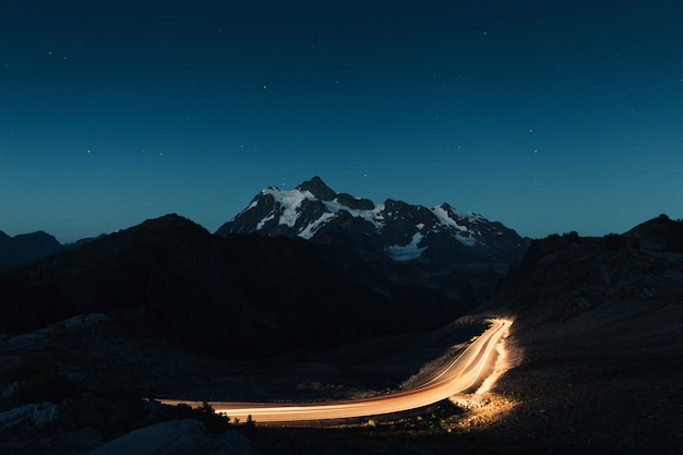 Free photo amazing night sky with a snowy rocky mountains in the middle and a dimly lit road