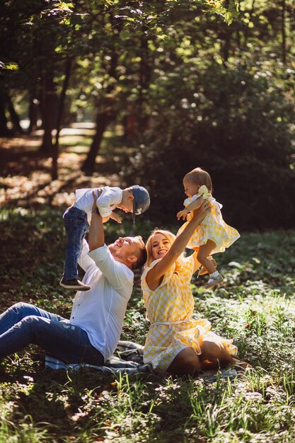 Amazing parents have fun with their two resting on a green lawn in park 