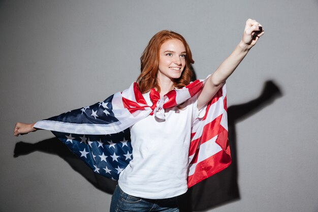 アメリカの国旗を持つ素晴らしい赤毛の若い女性のスーパーヒーロー