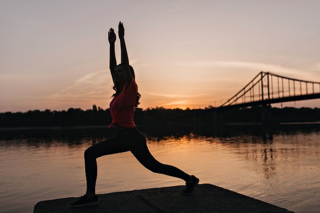 Amazing shapely girl doing yoga on sunrise. Lovely female model enjoying sunset views during training.