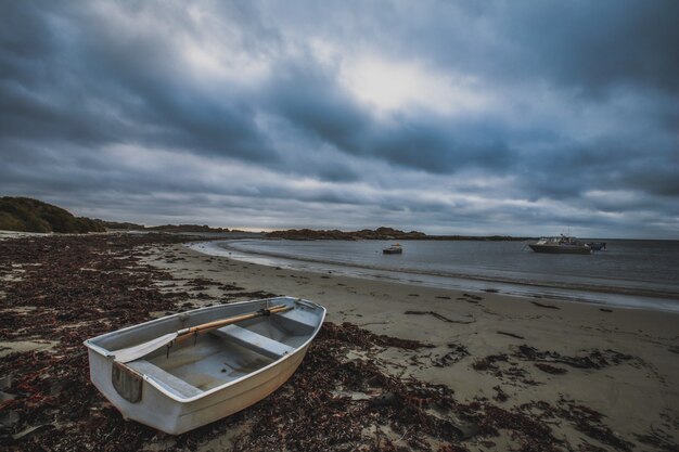 Amazing shot of an old boat on the sandy beach with calm ocean and other boats under the cloudy sky