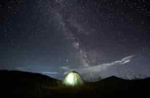 Free photo amazing starry night sky in the mountains and illuminated tent at campsite