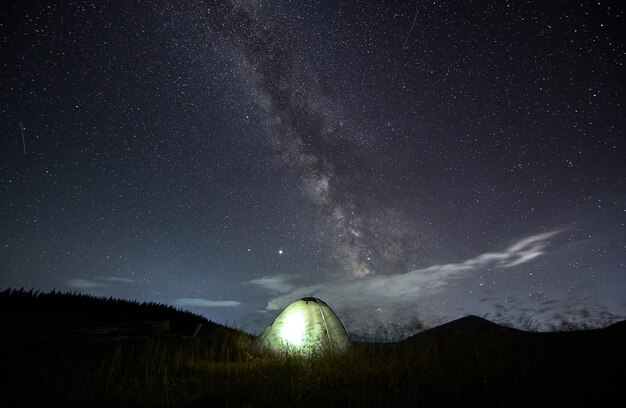 Удивительное звездное ночное небо в горах и освещенная палатка в кемпинге